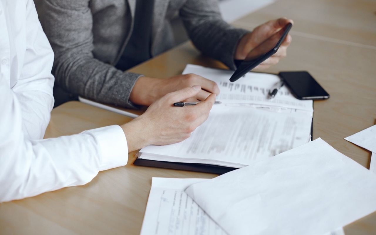 Dos personas firman documentos sobre la mesa de un despacho.