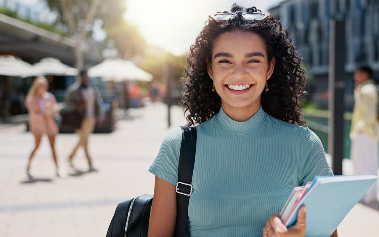 Una estudiante sonríe al aire libre con sus libros en el campus.