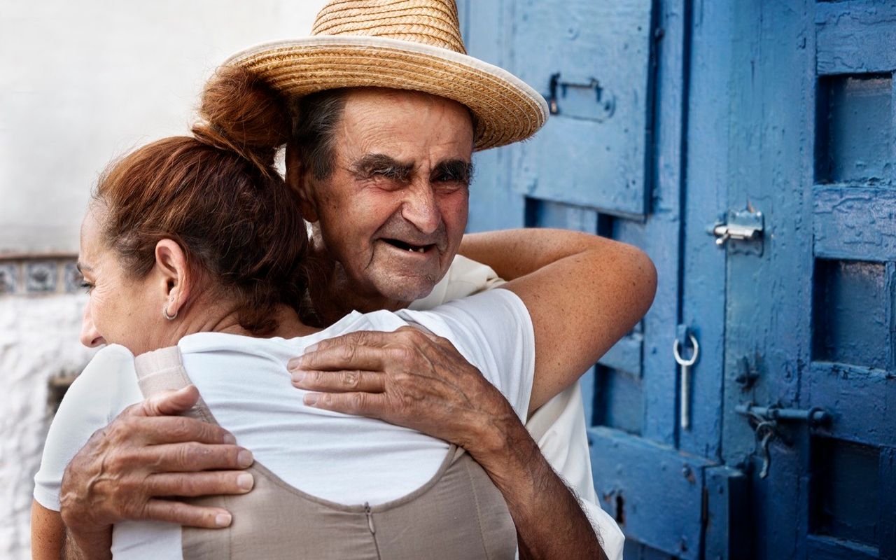 Un hombre mayor abraza a una mujer en la puerta de una casa.