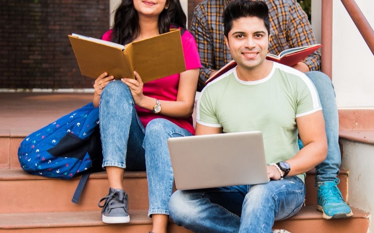 Un grupo de estudiantes estudia con libros y portátil en las escaleras del campus.