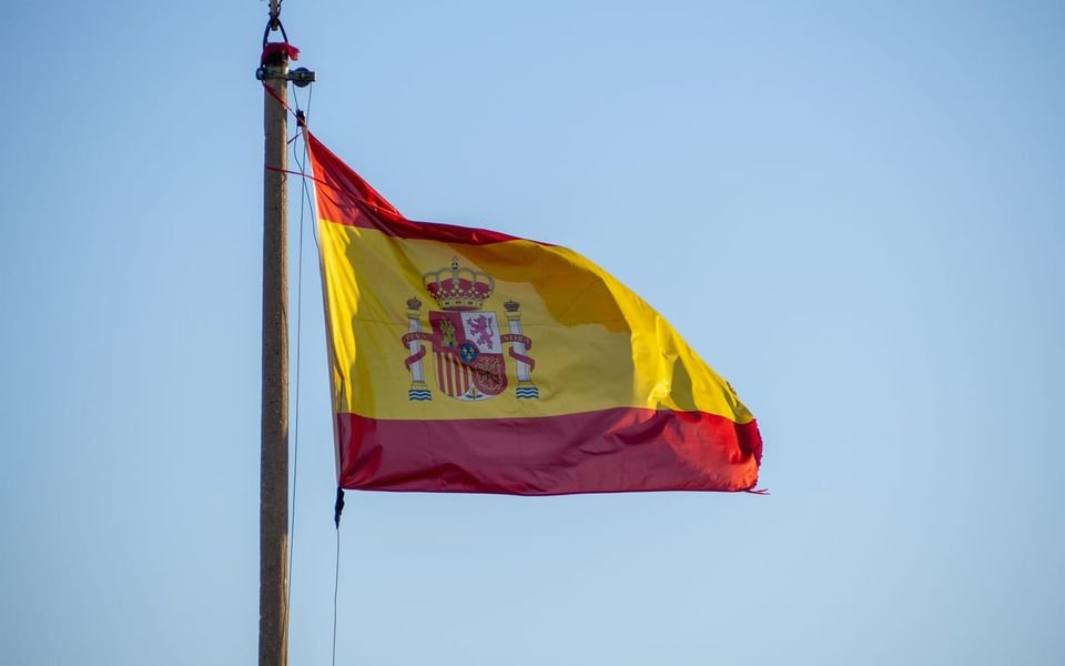 La bandera de España ondea en un mástil contra el cielo.