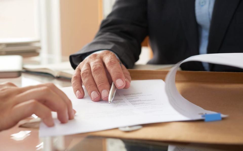Dos personas firman unos documentos sobre una mesa de despacho.