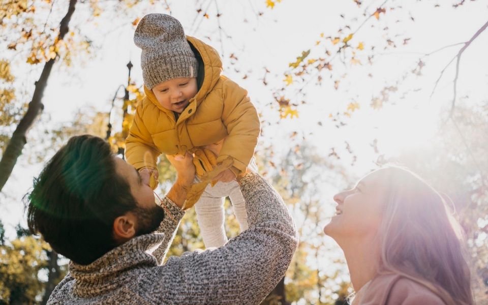Un padre y una madre sostienen a su bebé al aire libre.
