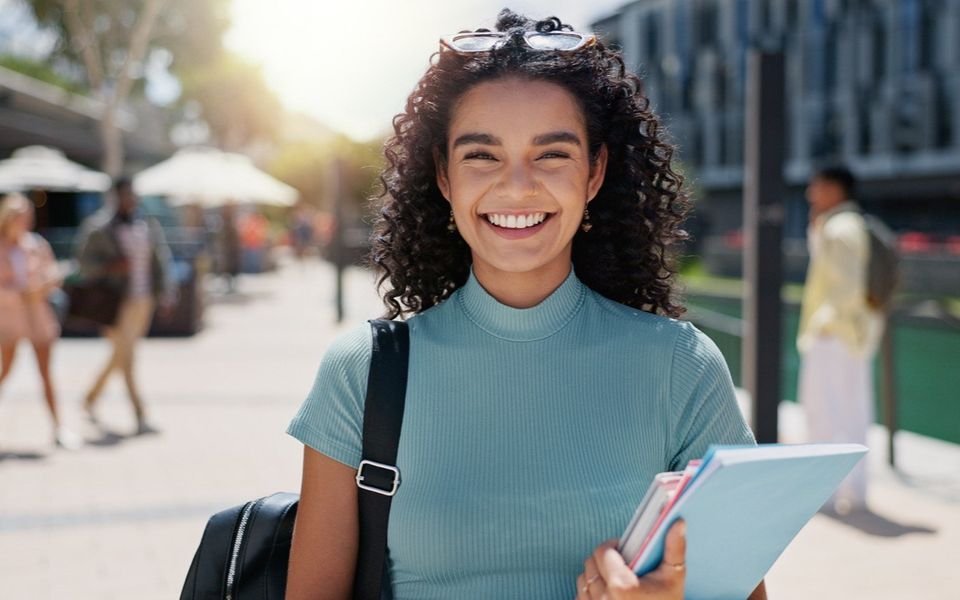 Una estudiante sonríe en el campus con sus libros.