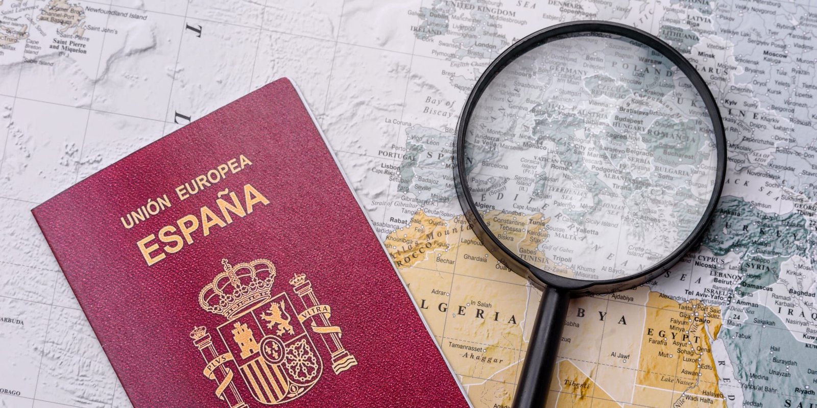Un pasaporte, una lupa y un mapa del mundo sobre una mesa.