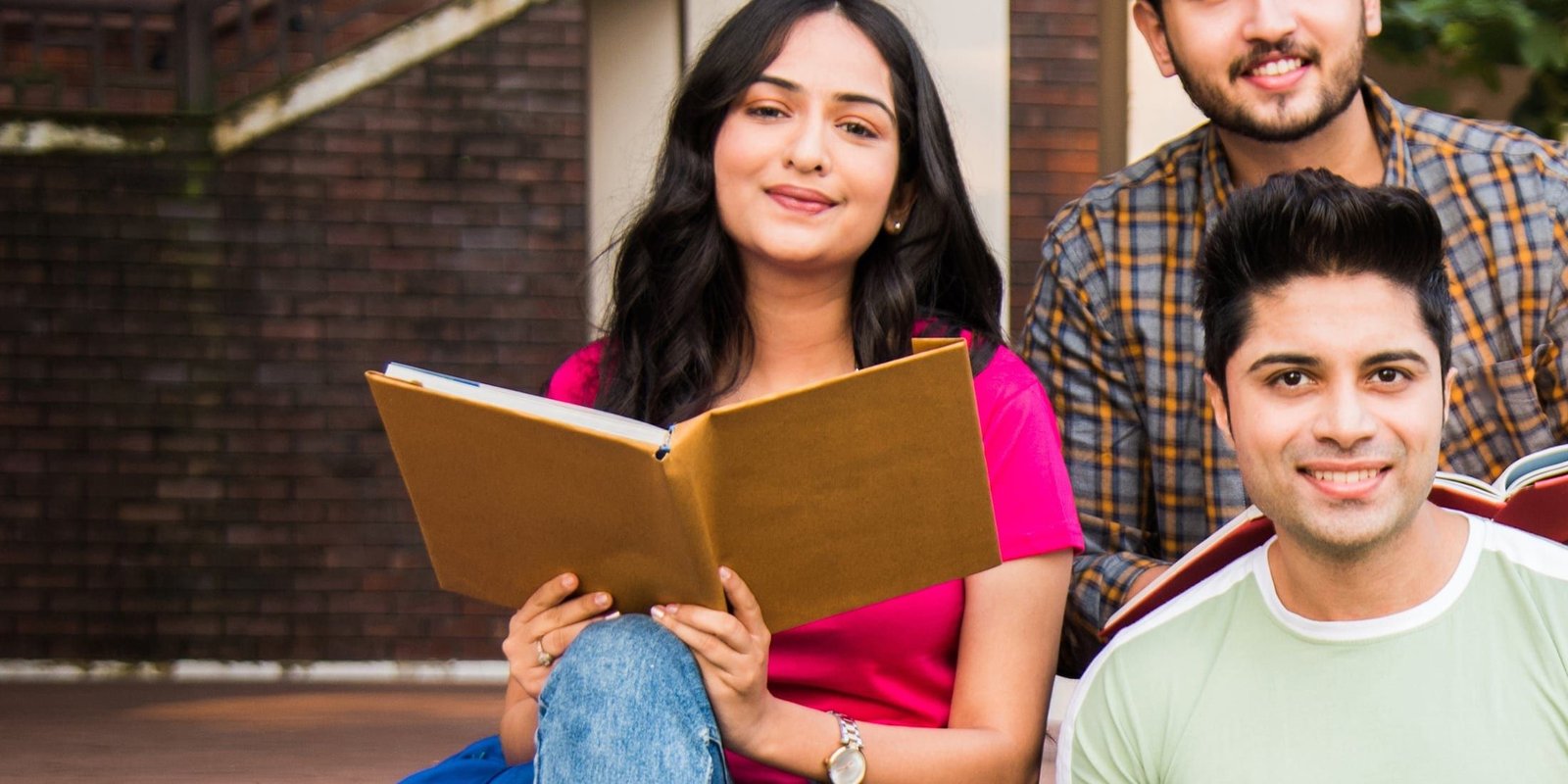 Un grupo de estudiantes estudia con libros y portátil en las escaleras del campus.